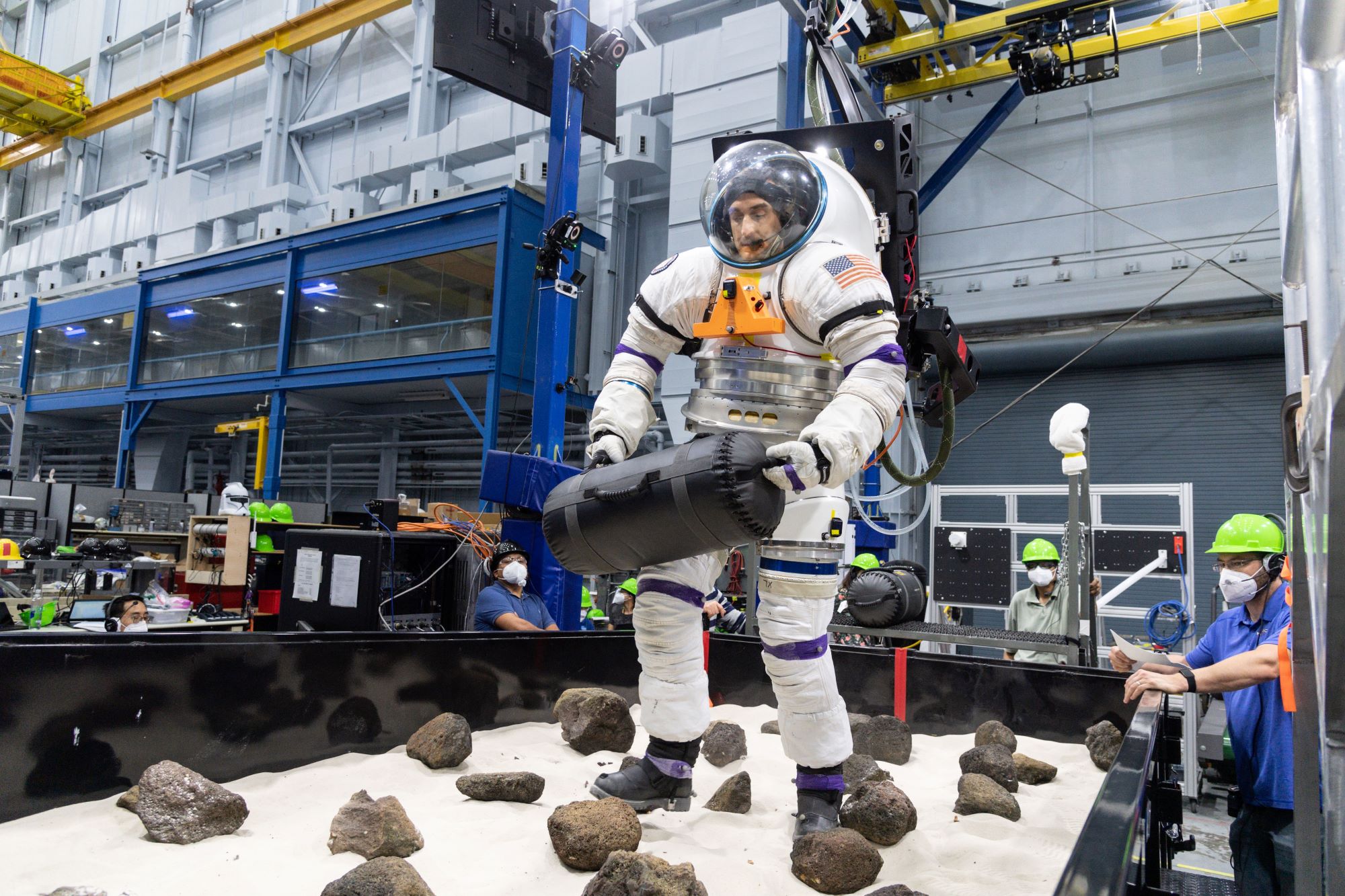 A volunteer from NASA’s Artemis Extravehicular Activity training group moves a 30-pound object through a boulder field while in a spacesuit connected to NASA’s Active Response Gravity Offload System, or ARGOS to test astronauts balance when they return to Earth from space.