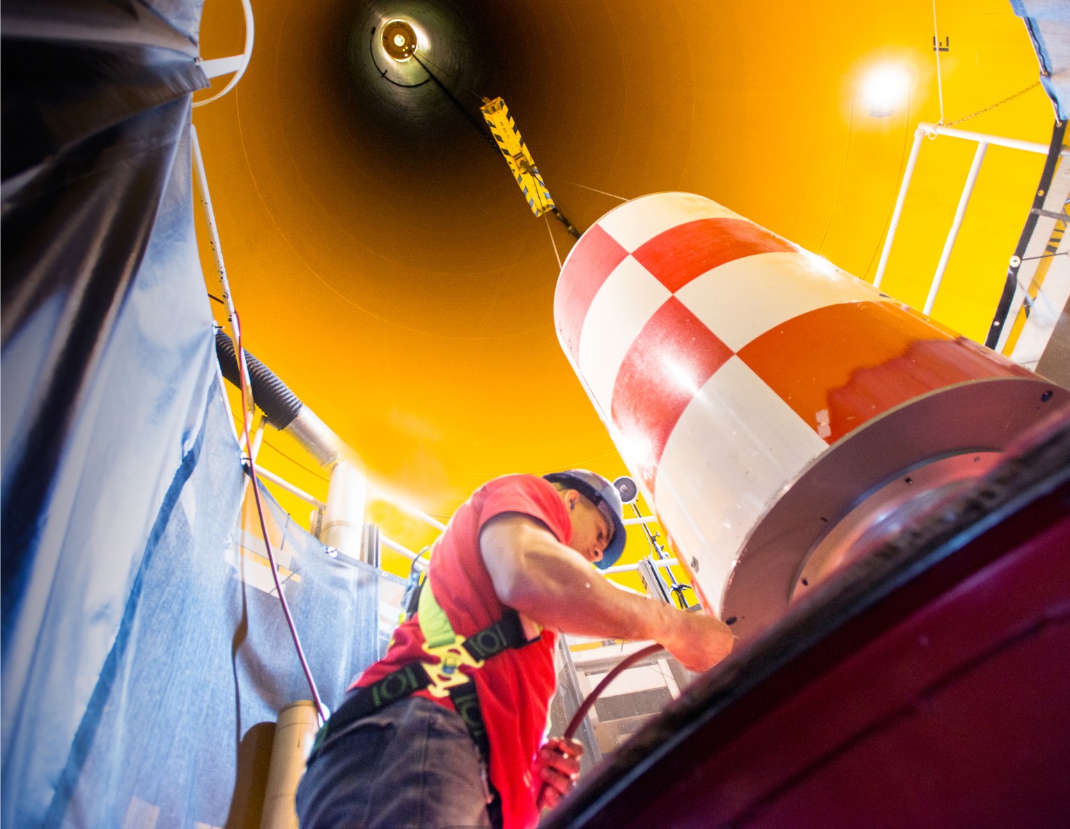 Technician at bottom of deep shaft with a metal canister attached to a crane.