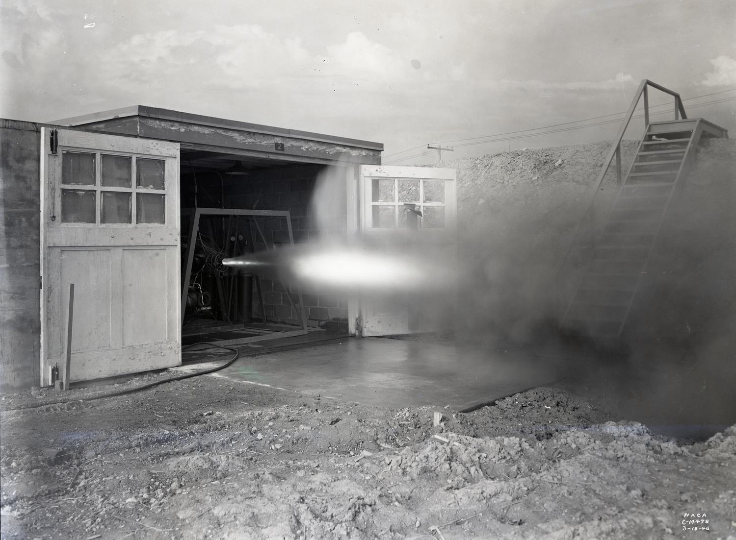 Rocket engine plume of fire and smoke blows out of old shed.