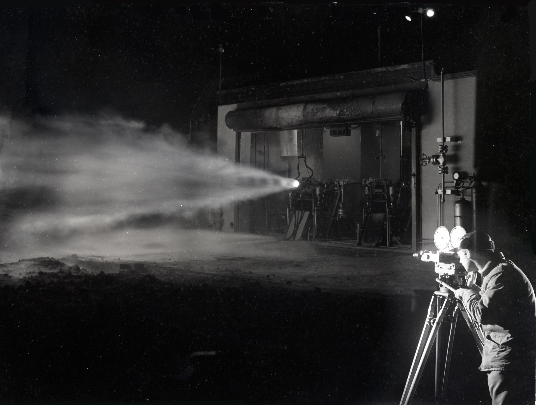 Film photographer looks through camera at rocket engine firing.