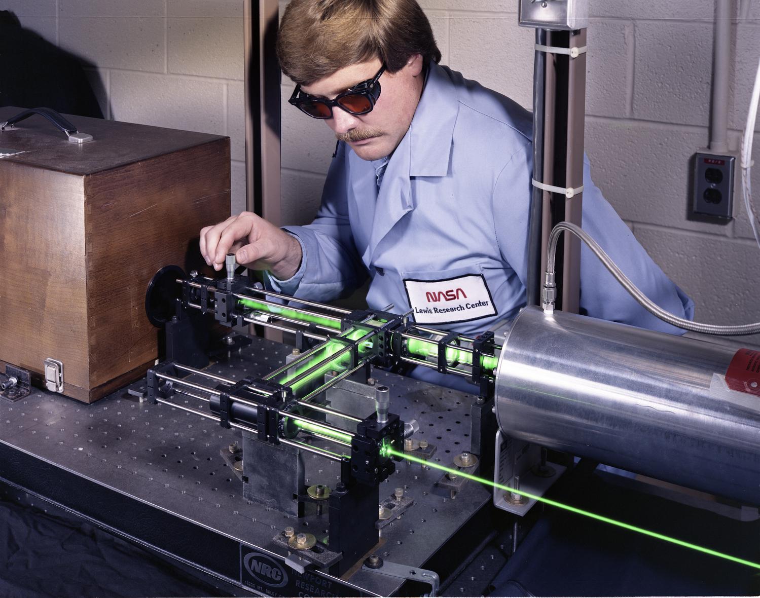 Researcher with protective glasses looks at laser emission through series of small pipes.