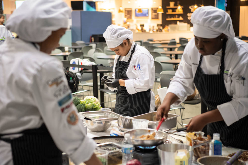 Student chefs prepare a meal at a table.