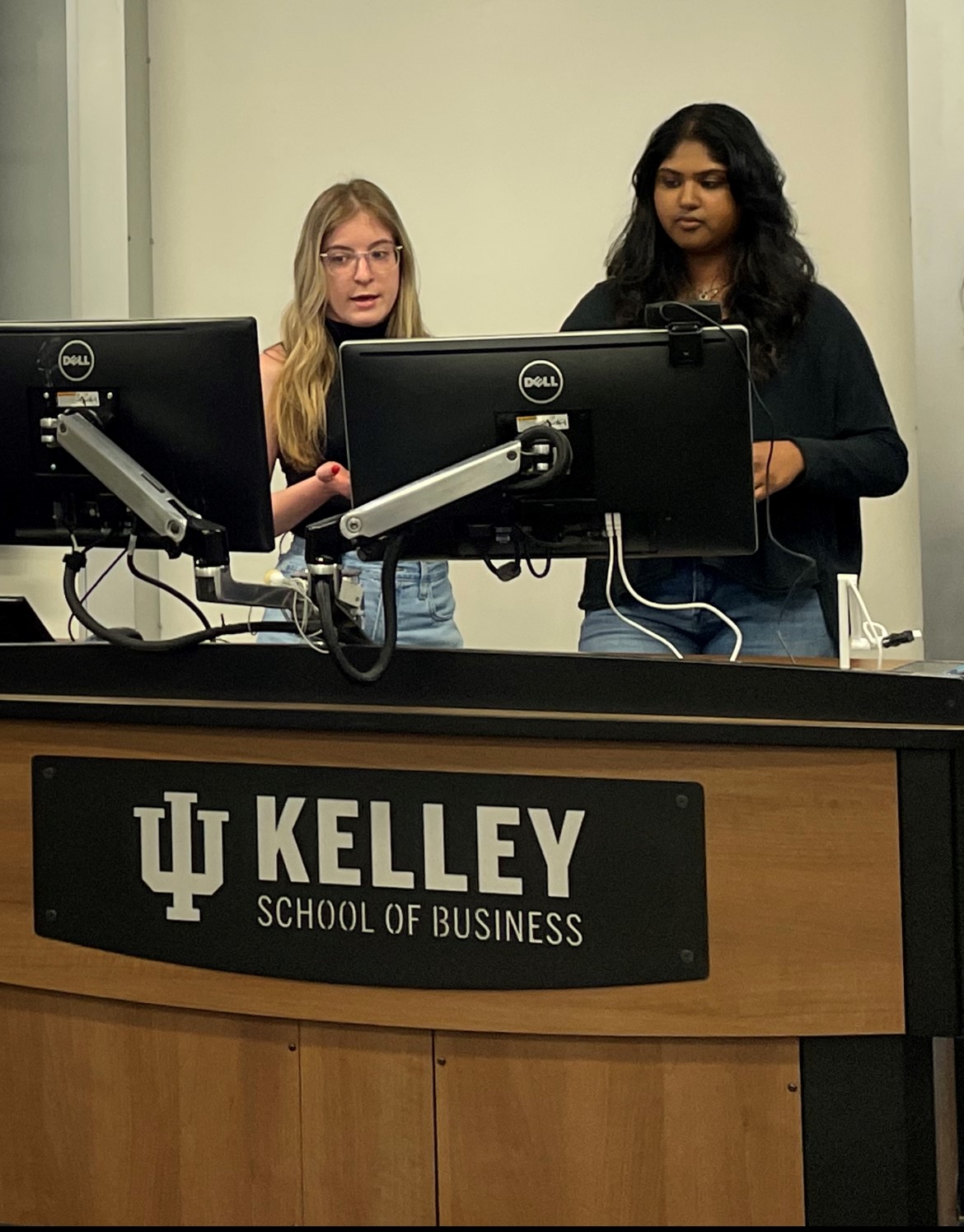 Two female students look at computer screens at the front of a class.