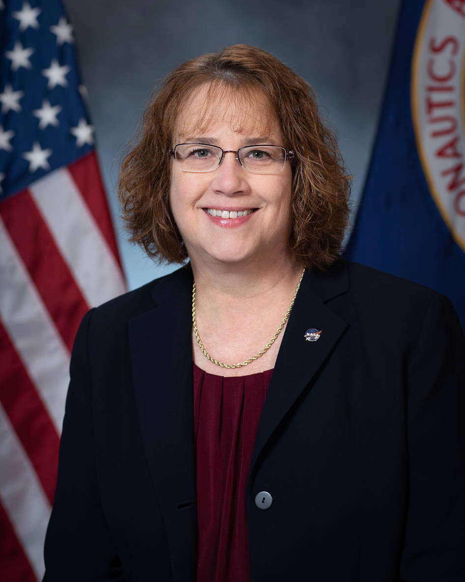 Portrait of Dawn Schaible with U.S. flag behind her on the left and NASA flag on her right.