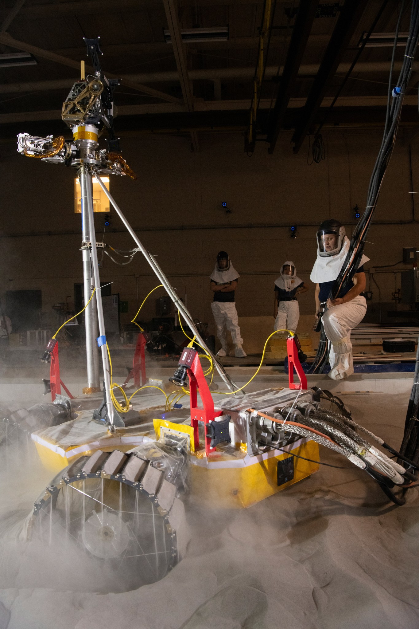 Researchers in protective equipment work with the VIPER rover prototype in lunar simulant soil in the SLOPE lab at Glenn.