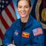 A smiling female astronaut in a blue jump suit