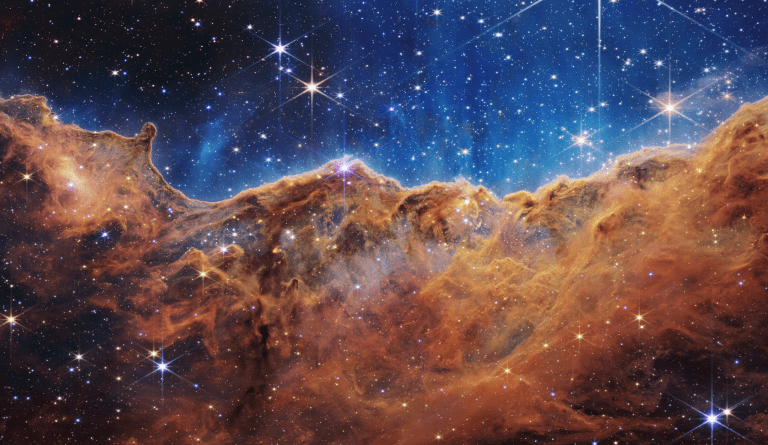 Este paisaje de "montañas" y "valles" salpicados de estrellas brillantes es en realidad el borde de una región cercana, joven y de formación estelar llamada NGC 3324 en la Nebulosa Carina. Capturada en luz infrarroja por el nuevo Telescopio Espacial James Webb de la NASA, esta imagen revela por primera vez áreas previamente invisibles del nacimiento de estrellas. Créditos: NASA, ESA, CSA y STScI