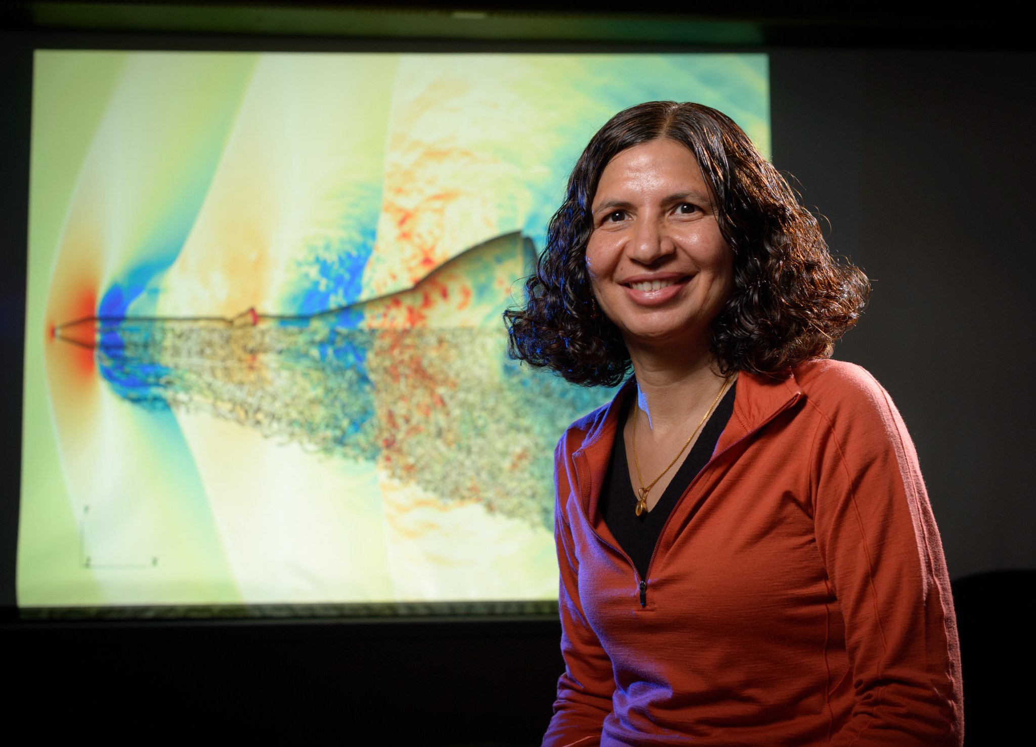 A person stands in front of a screen showing computer simulations of Orion launch abort system.