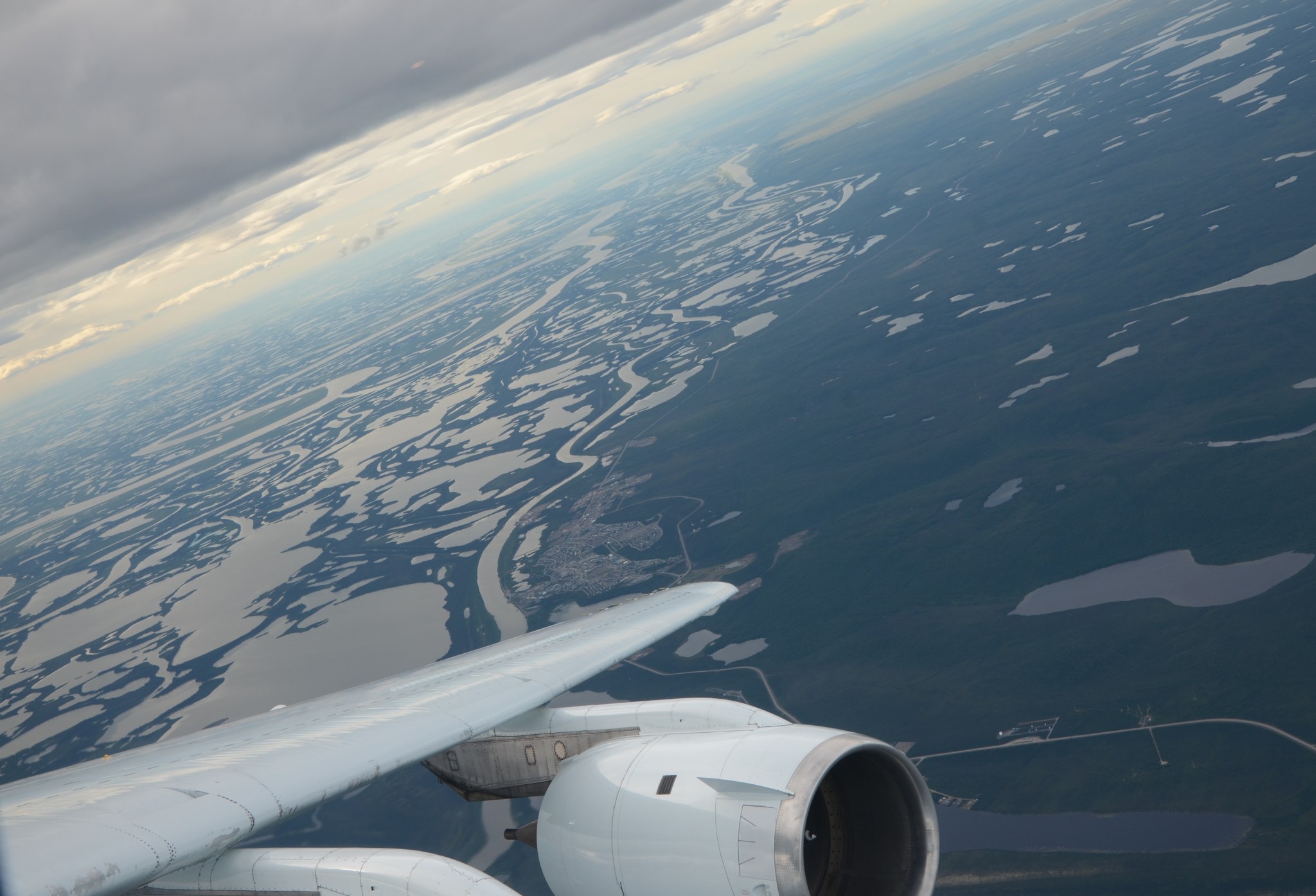 As seen from aboard NASAs DC-8 aircraft: A plane's wing is visible in the lower portion of this photo, which shows an askew view of a sinuous river and surrounding ponds, looking gray as they reflect the light. The surrounding landscape, a deep blue-green