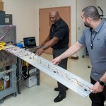Allen Parker, Fiber Optic Sensing System (FOSS) senior research engineer at NASA’s Armstrong Flight Research Center in California, and Jonathan Lopez show how FOSS in aeronautics is used on a wing to determine its shape and stress on its structure.