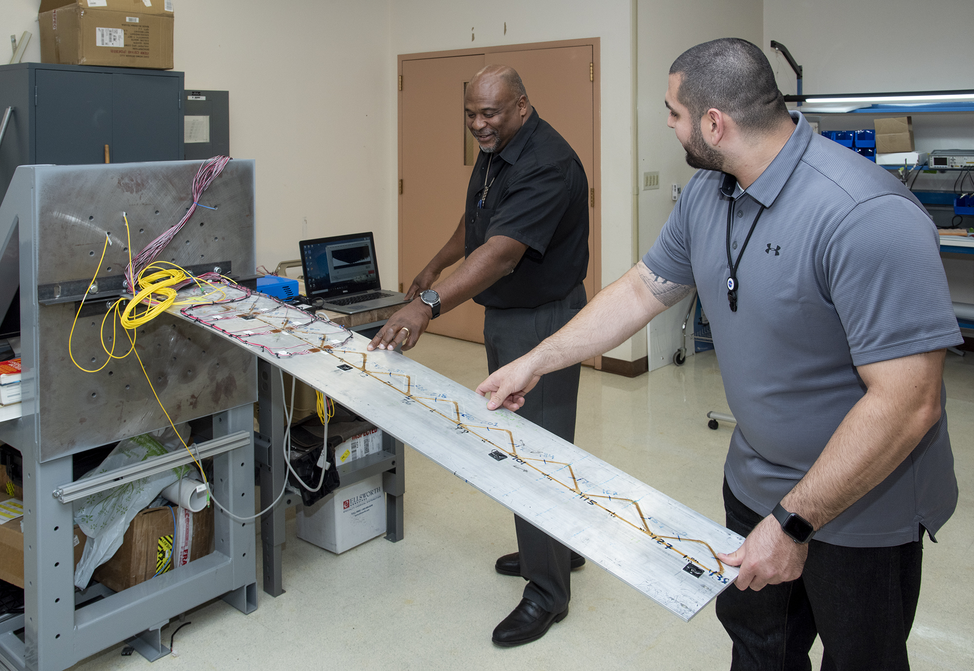 Allen Parker, Fiber Optic Sensing System (FOSS) senior research engineer at NASA’s Armstrong Flight Research Center in California, and Jonathan Lopez show how FOSS in aeronautics is used on a wing to determine its shape and stress on its structure.