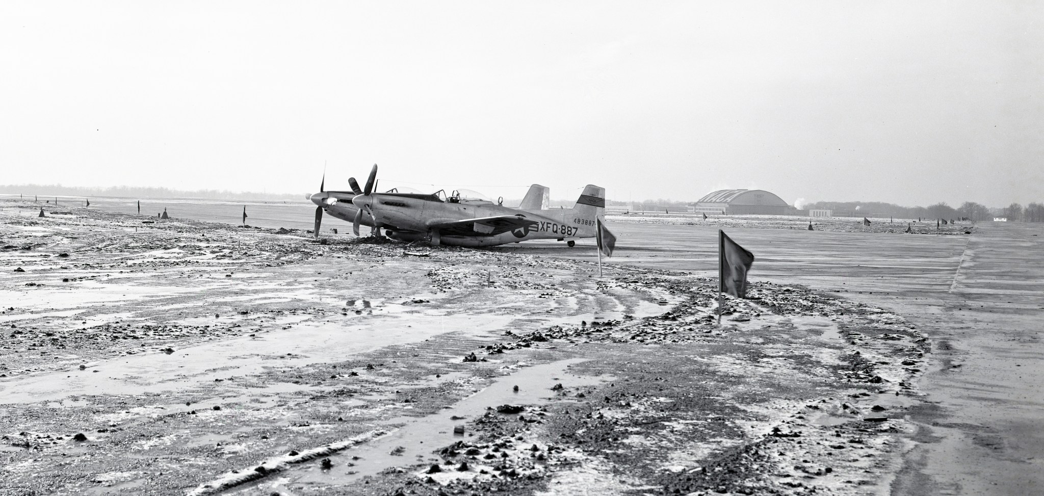 Front end of airplane is sunken in mud while back end sits on icy runway.