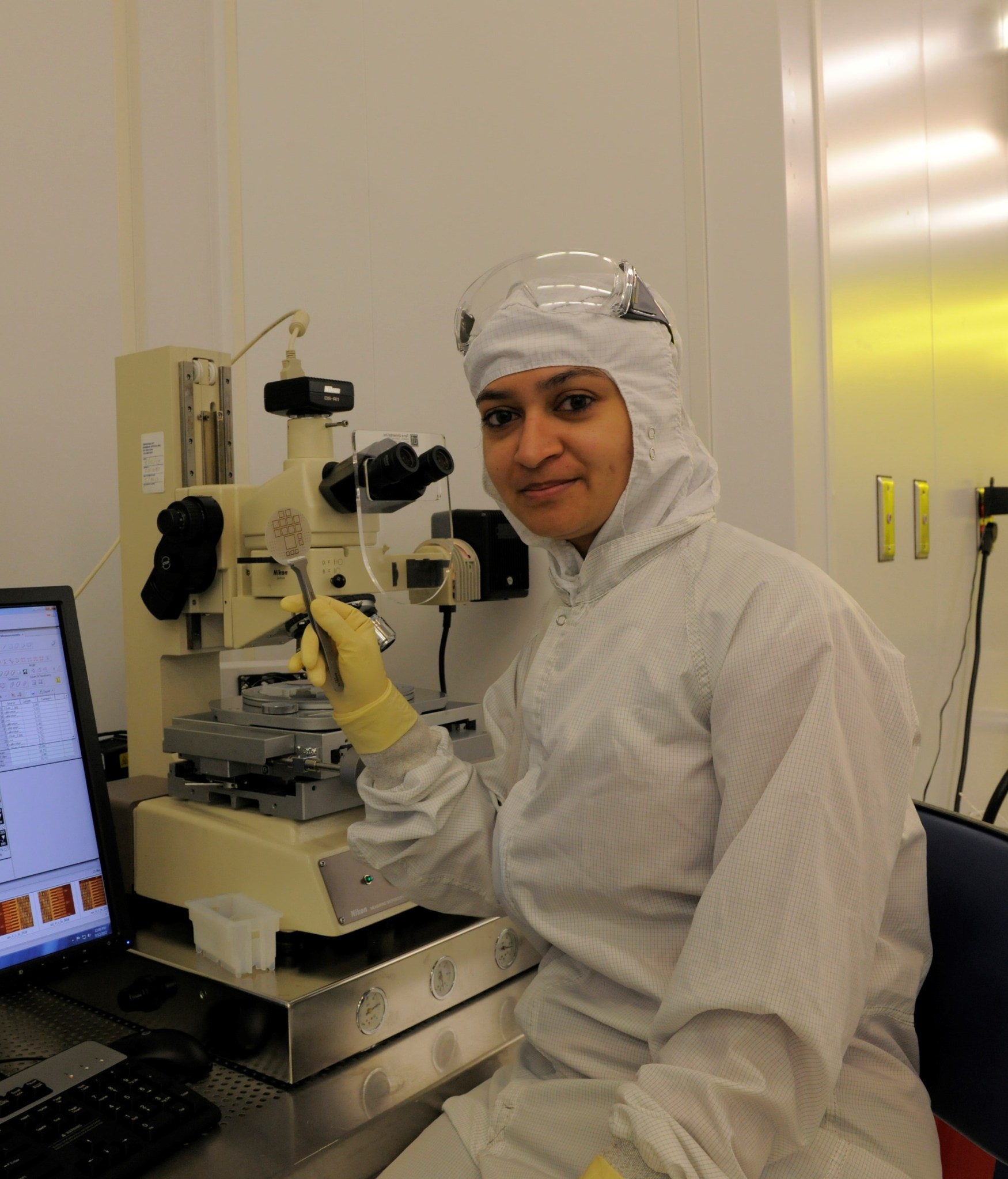 woman in white protective clothing sits in a lab by a computer