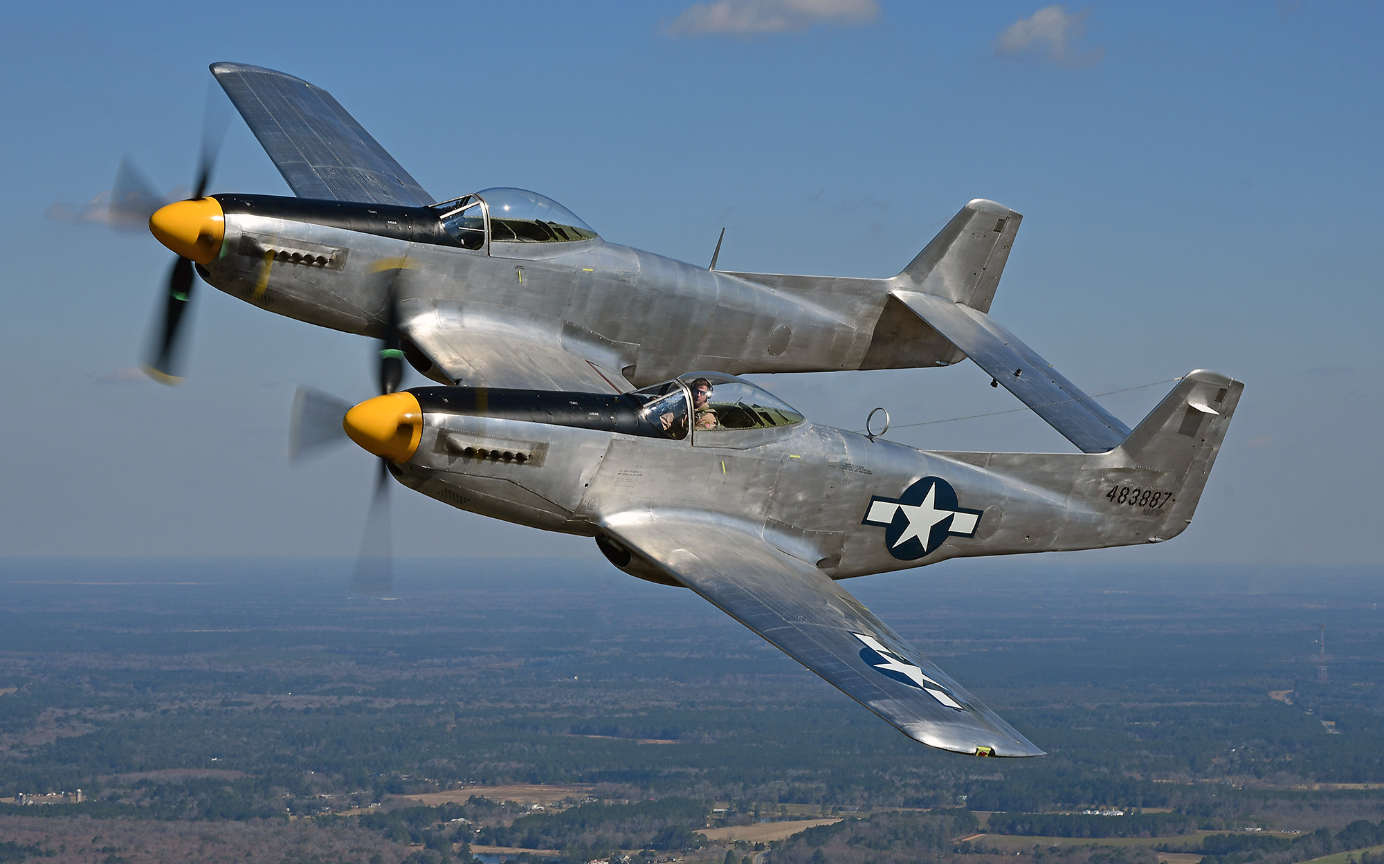 Military aircraft flies at an angle above land in the background.