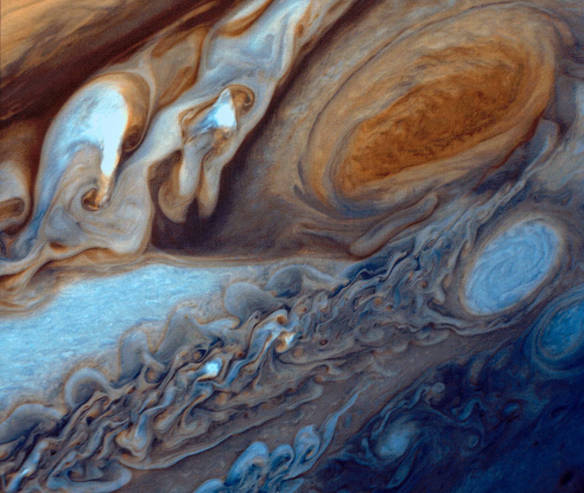 Jupiter's Great Red Spot is a swirl of orange-brown, lightening to pale orange at the outer edges. To its left are brown, white, and orange swirls; at bottom, blue and white swirls and ripples. The entire image has the effect of dyes dripped into water.