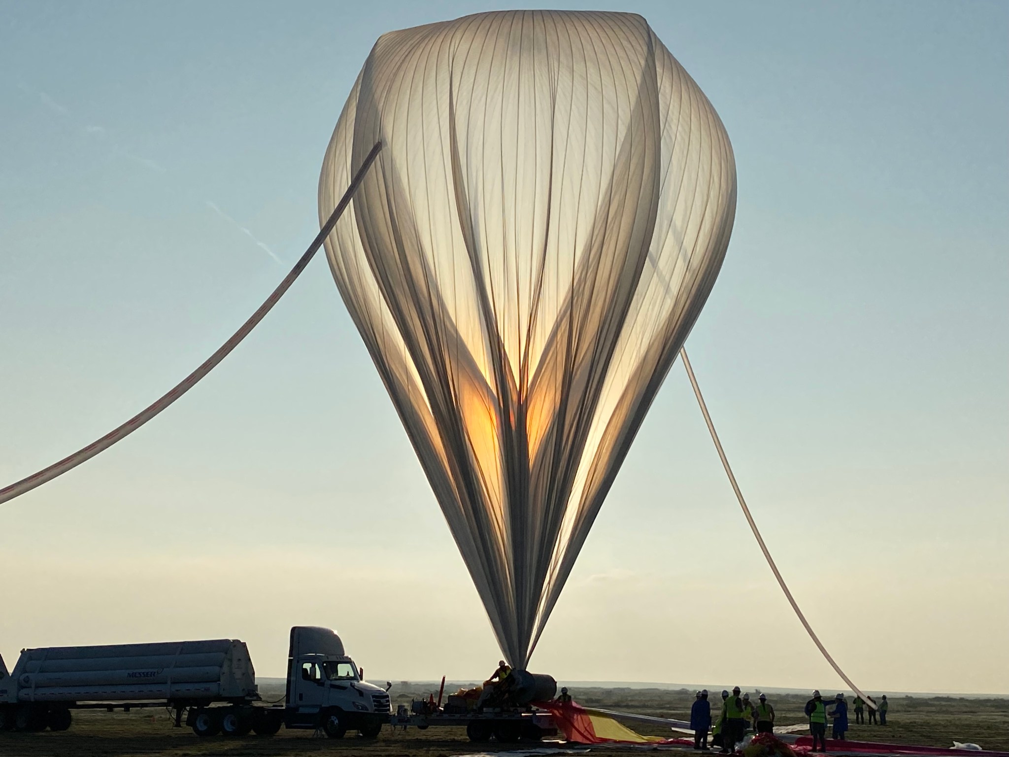 An upside-down, teardrop-shaped large balloon is partially inflated against a soft blue sky.