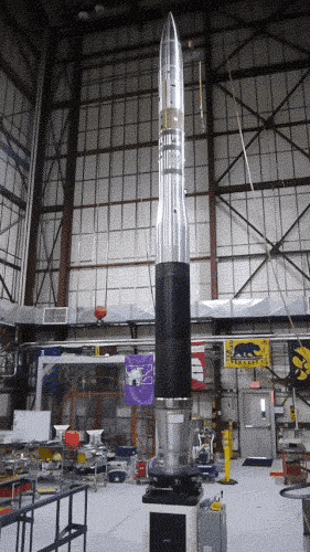 A rocket standing vertically in a large hangar, rotating.