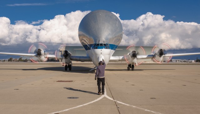 The Super Guppy lands on the runway at Moffett Field at NASA's Ames Research Center in Silicon Valley, California. A person stands in front of the aircraft, directing it.