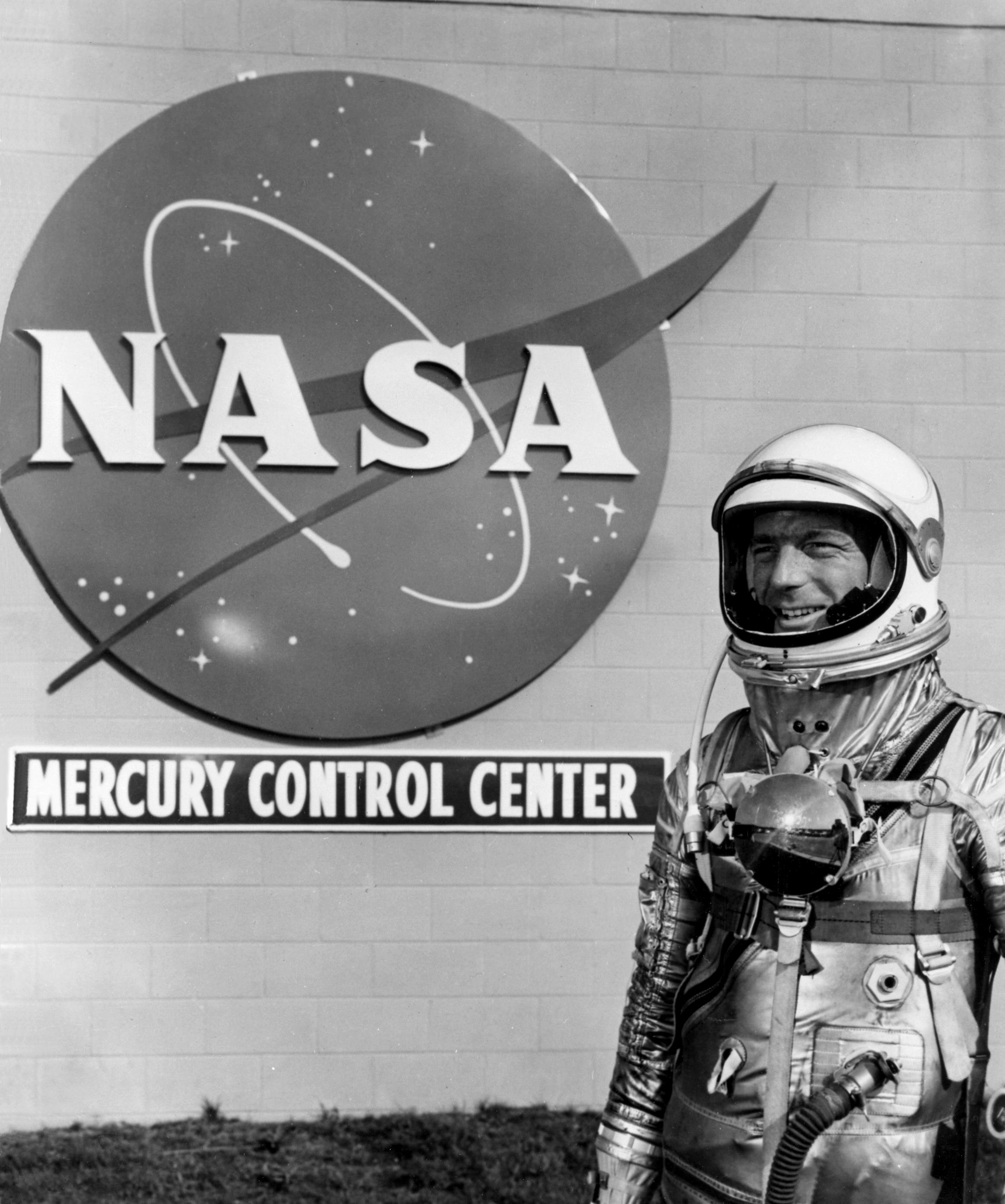 Astronaut Scott Carpenter poses in his flight suit in front of the NASA logo on the side of the Mercury Control Center at Cape Canaveral