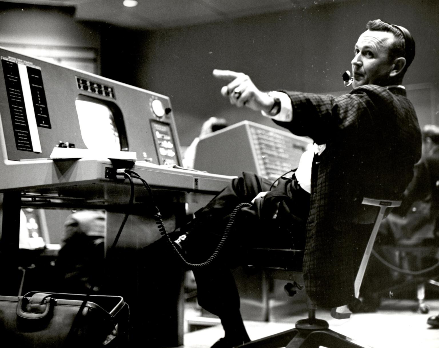 Flight Director Chris Kraft at his console at the Mercury Control Center pointing off to the left beyond the shot of the photo. Black and White Image.