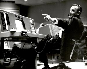 Flight Director Chris Kraft at his console at the Mercury Control Center pointing off to the left beyond the shot of the photo. Black and White Image.