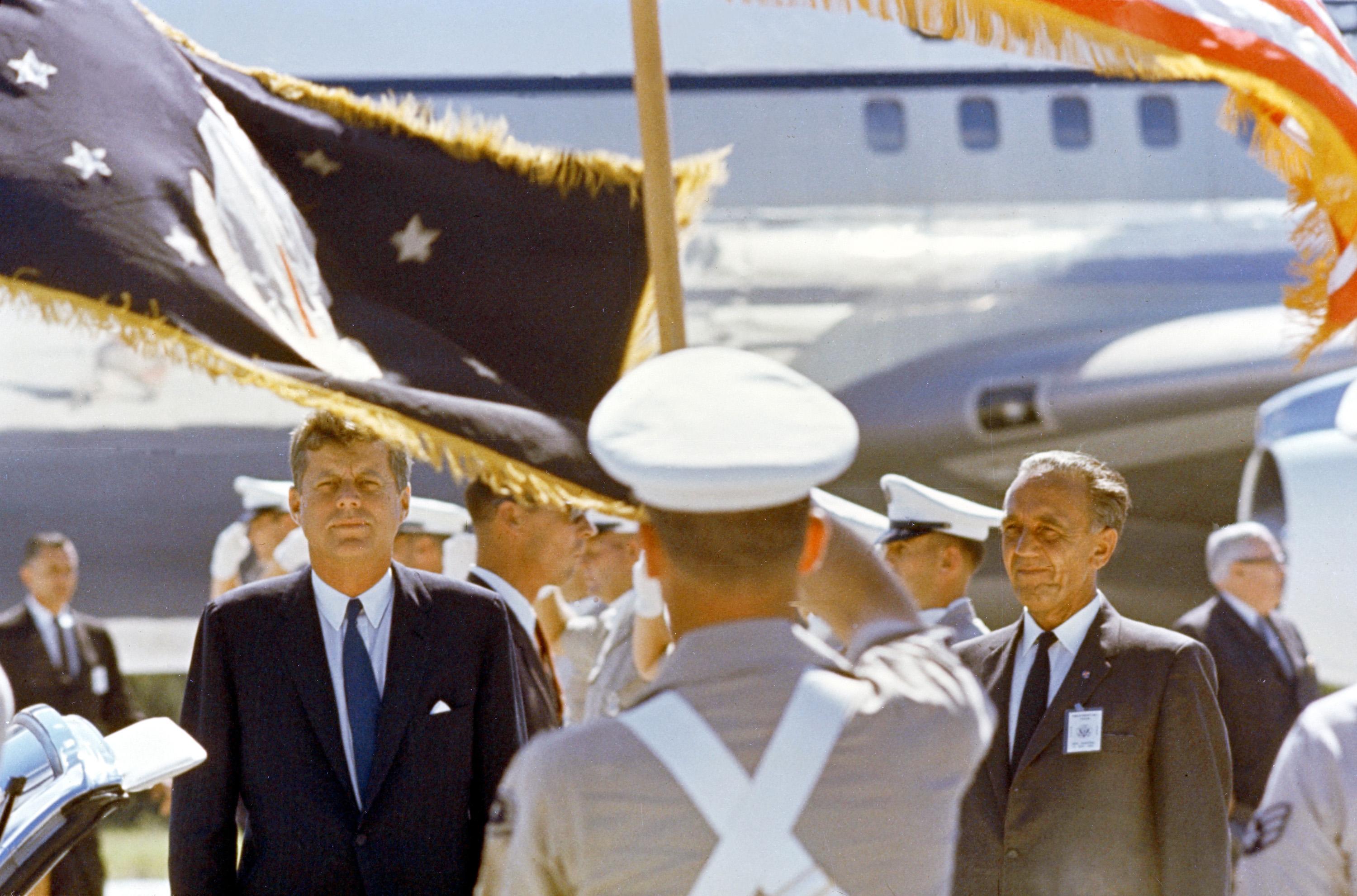 On Sept. 11, 1962, President John F. Kennedy is welcomed by a color guard and Center Director Kurt Debus (right). An airplane appears in the background.
