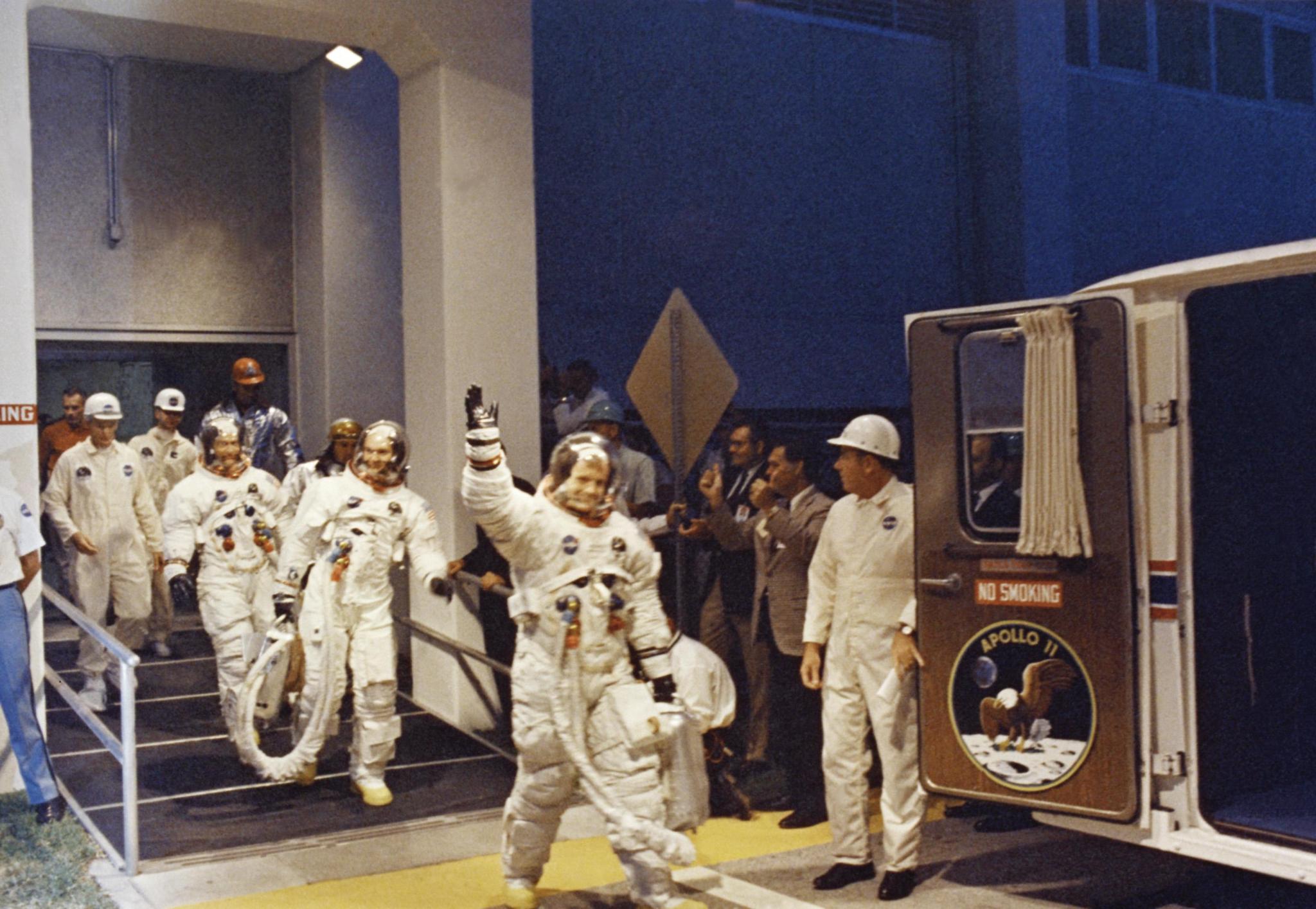 On July 16, 1969, Apollo 11 Commander Neil A. Armstrong waves as he leads astronauts Michael Collins and Edwin E. Aldrin, Jr., from the Manned Spacecraft Operations Building to the transfer van for the eight-mile trip to Pad 39A.