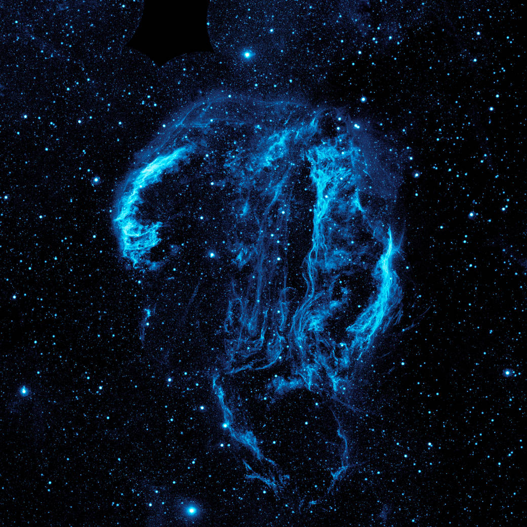 image of plumes of gas and dust in blue coloring against the night sky.