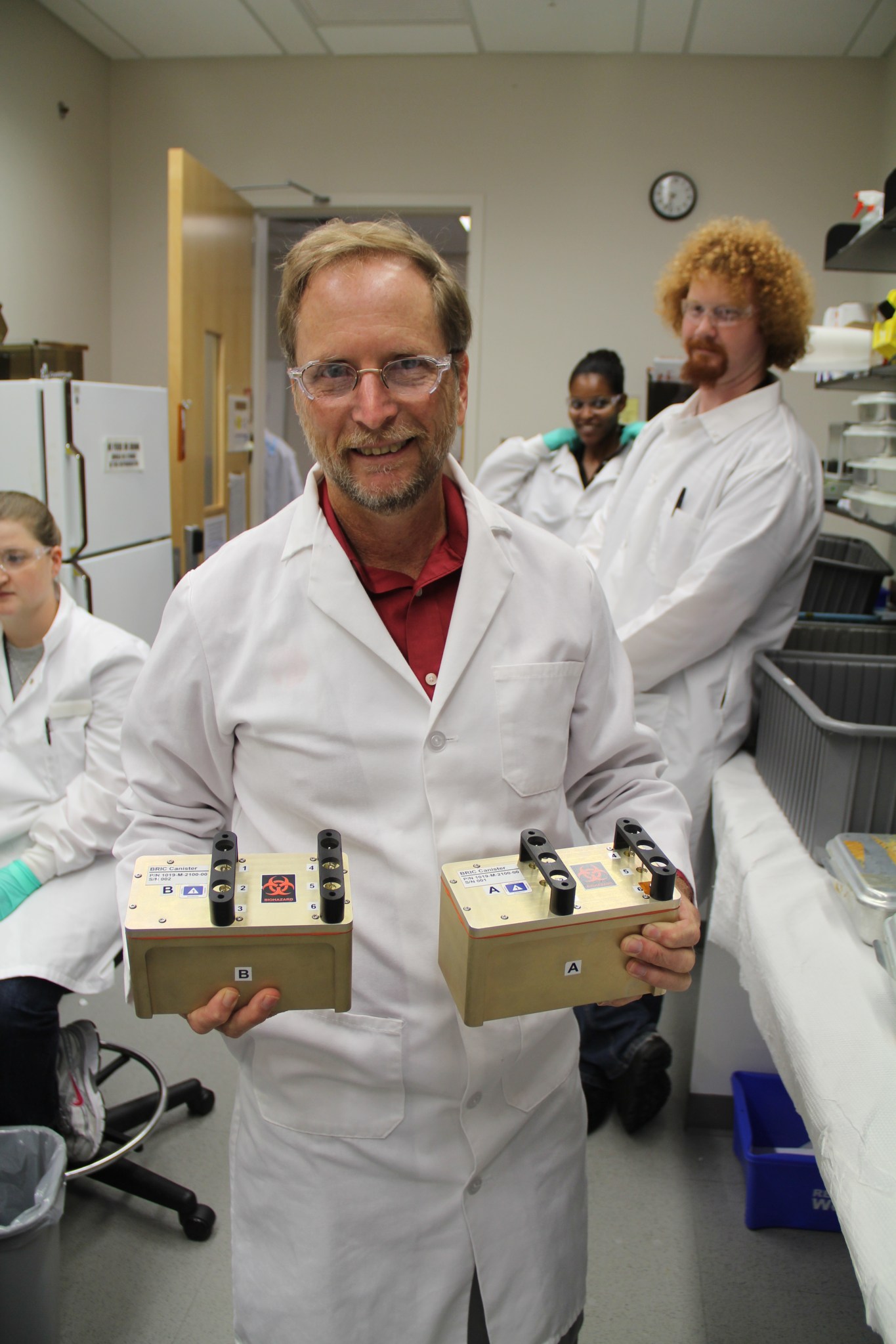 Scientist in a lab setting with 3 other scientists in the background.