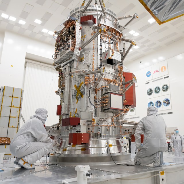 Two technicians in white ?bunny suits? work on the Europa Clipper spacecraft inside of a clean room