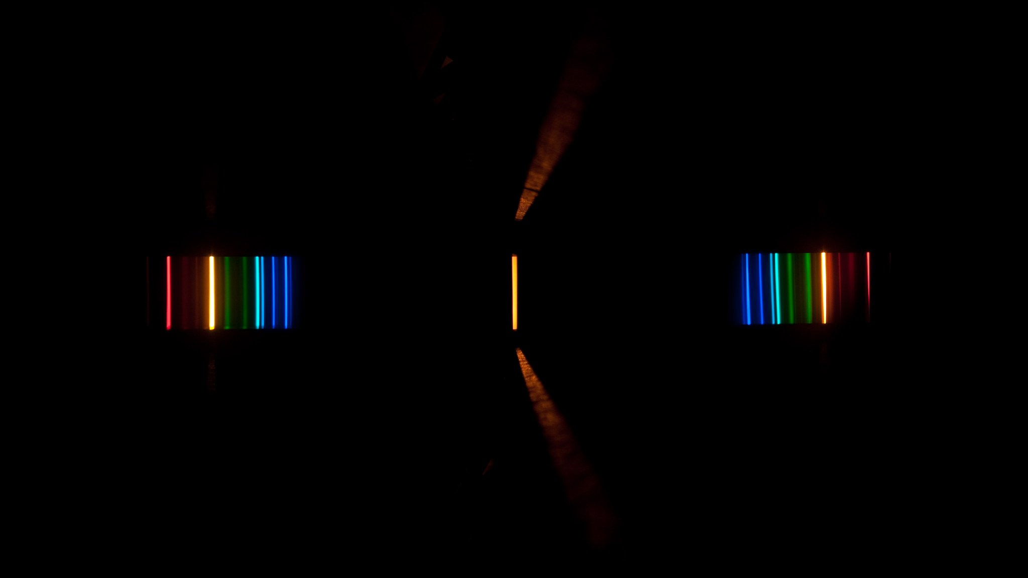 Central light beam and a rainbow series of beams to its left and right against a black background.