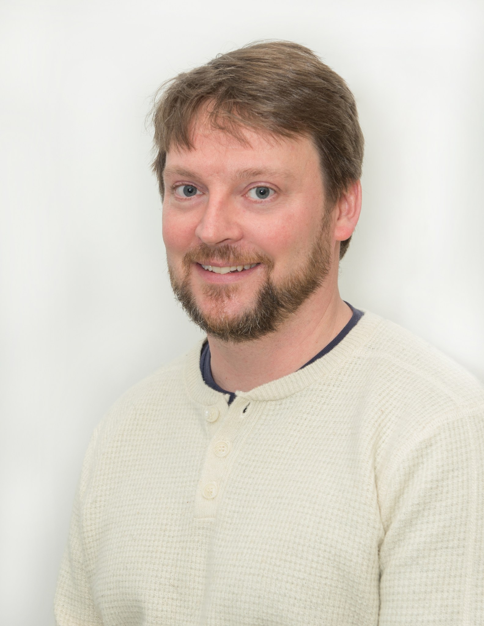 A man with blond hair and beard smiles at the camera in a portrait.