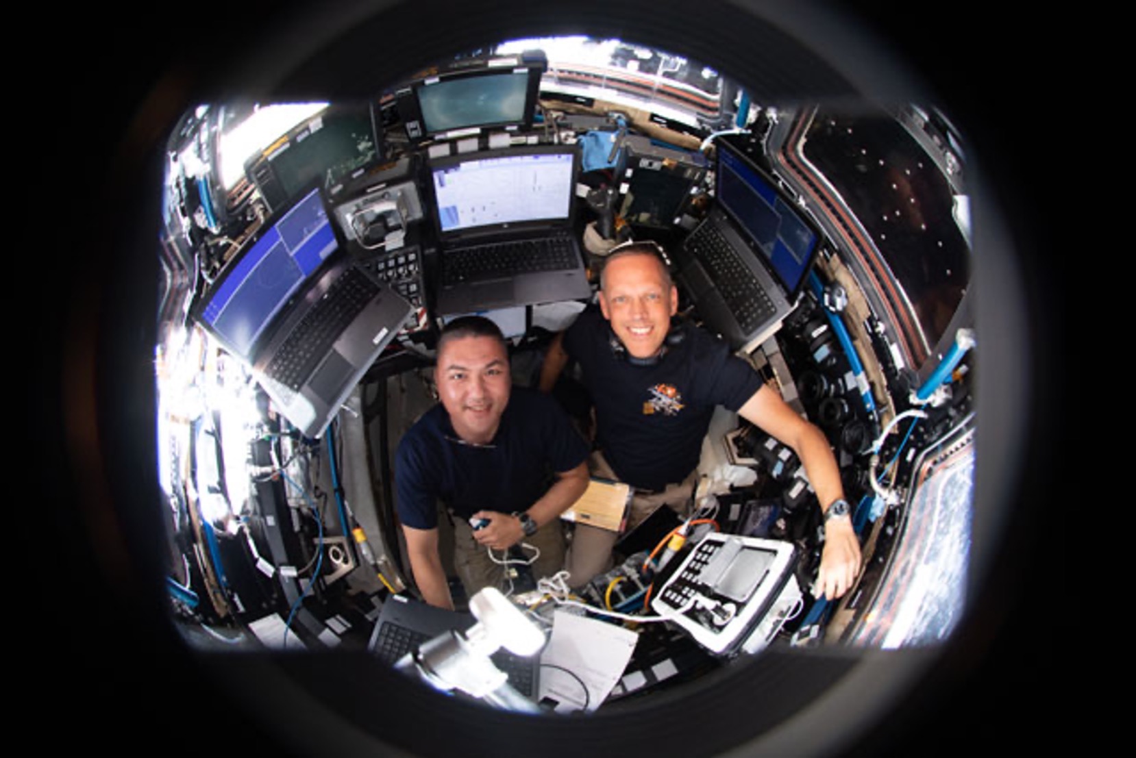 NASA astronauts Kjell Lindgren and Bob Hines are pictured inside the International Space Station's seven-windowed cupola monitoring the approach and rendezvous of Boeing's CST-100 Starliner spacecraft on the company's Orbital Flight Test-2 mission.