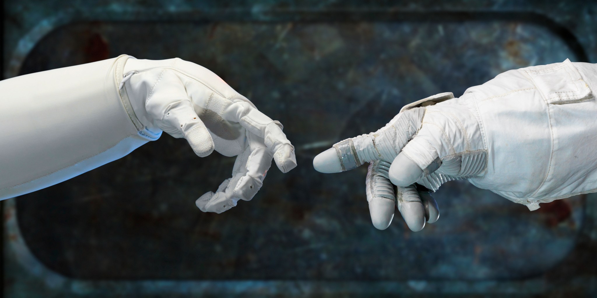 Robotic hand reaching out to touch a human's hand wearing a spacesuit glove