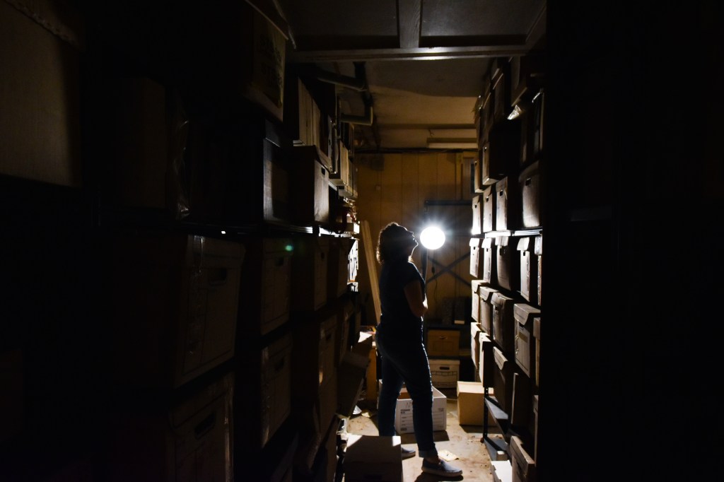 Archivist looks up at boxes stacked on shelves