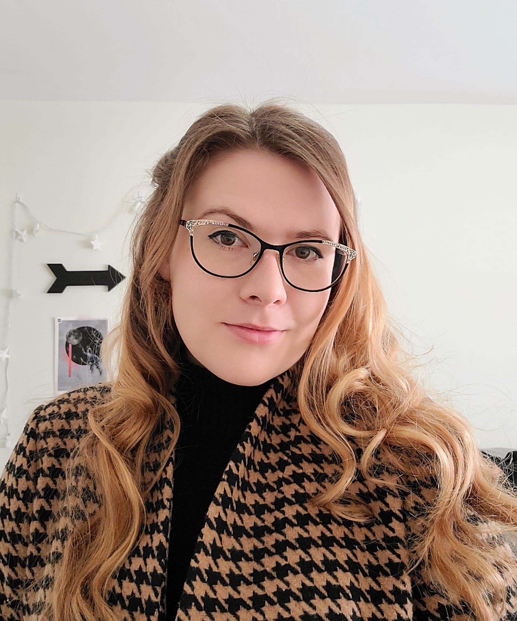 Elizabeth Tammi, a woman with glasses and long blonde hair, smiles at the camera for a selfie.