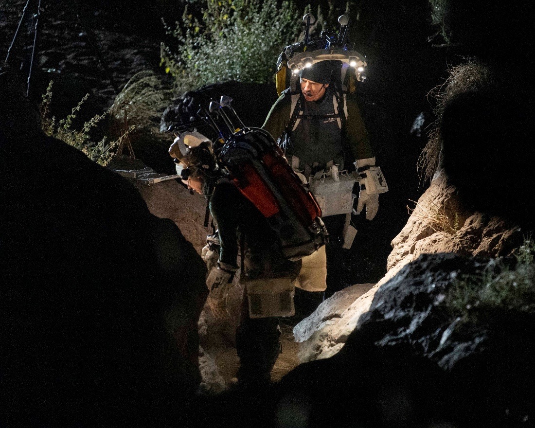 Nighttime photo of NASA astronauts Zena Cardman and Drew Feustel exploring a volcanic geologic outcrop while wearing spacewalk backpacks.