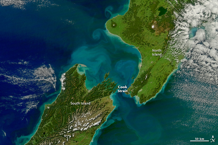 A view of sediment flowing in the Pacific Ocean, showing New Zealand's North and Southern Islands, captured by NASA’s Aqua satellite. The coasts of both islands are surrounded by turquoise water, with swirls extending further into the ocean, where they fade darker blue.