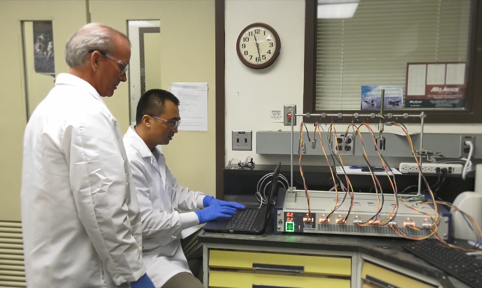 Two researchers using a cyclic voltameter to check their solid-state battery.