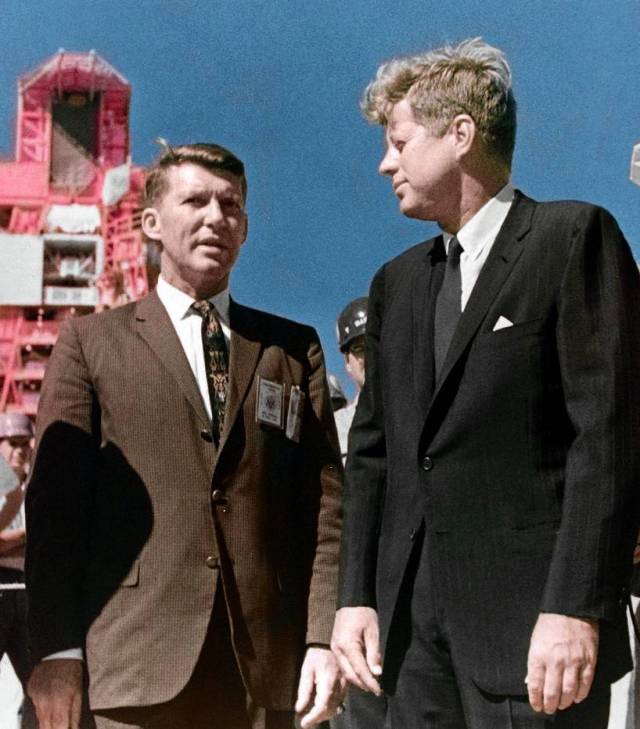 Wally Schirra and President John F. Kennedy talking in front of a rocket launch structure.
