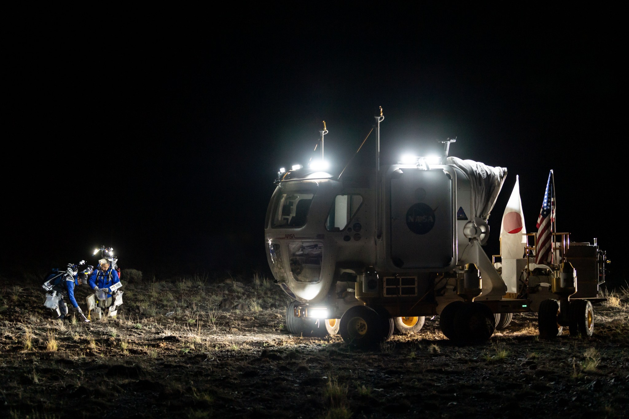 D-RATS JAXA crew members Akihiro Hoshide and Yusuke Yamasaki collect samples during a simulated moonwalk using light from the rover and their backpacks.