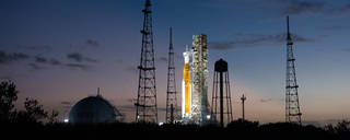 NASA’s Space Launch System (SLS) rocket with the Orion spacecraft aboard is seen illuminated by spotlights after sunset atop the mobile launcher at Launch Pad 39B .