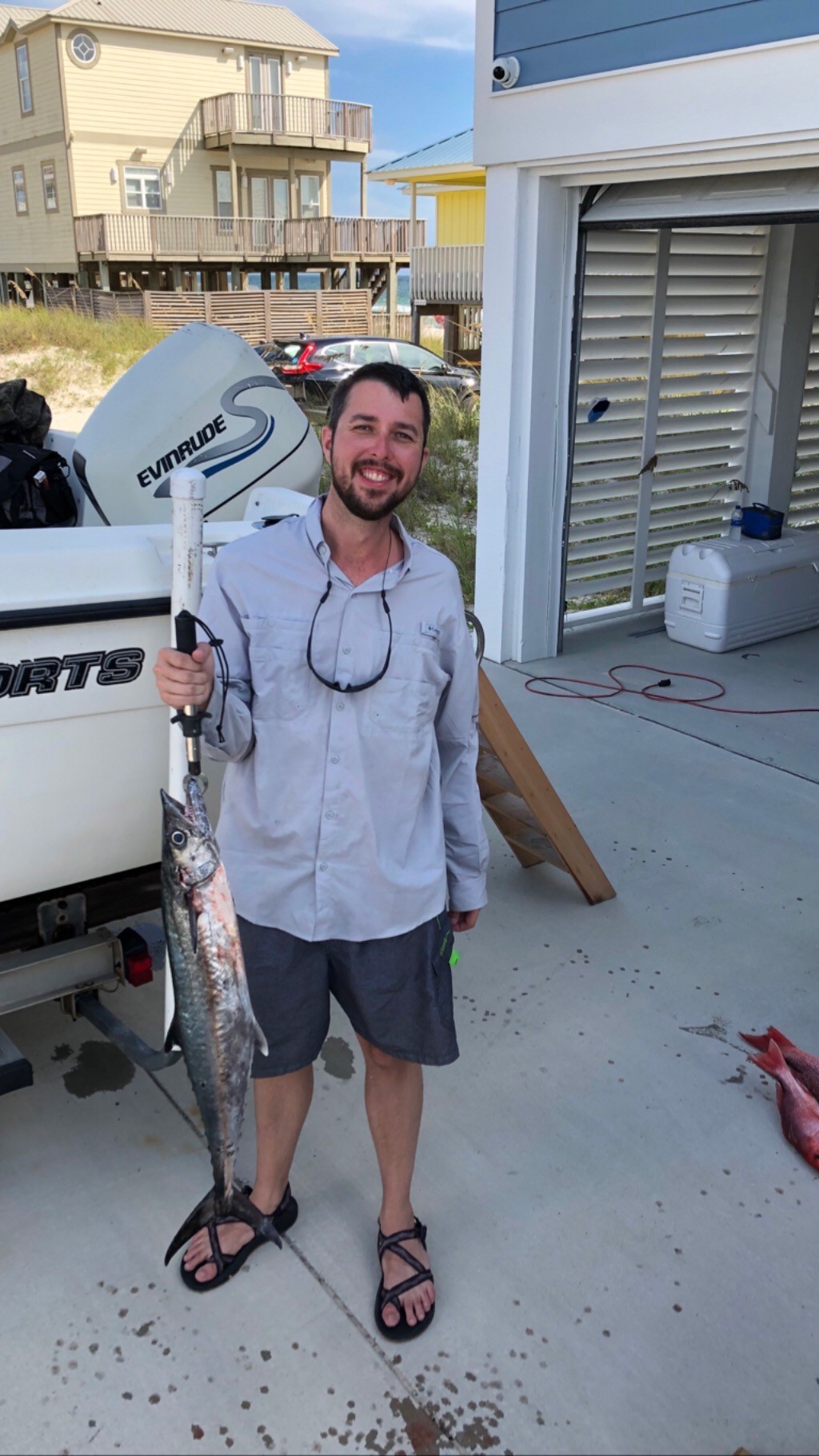 Jordan Bell, a research scientist at NASA’s Marshall Space Flight Center, stands by a boat in a driveway with a fish he caught in his hand.