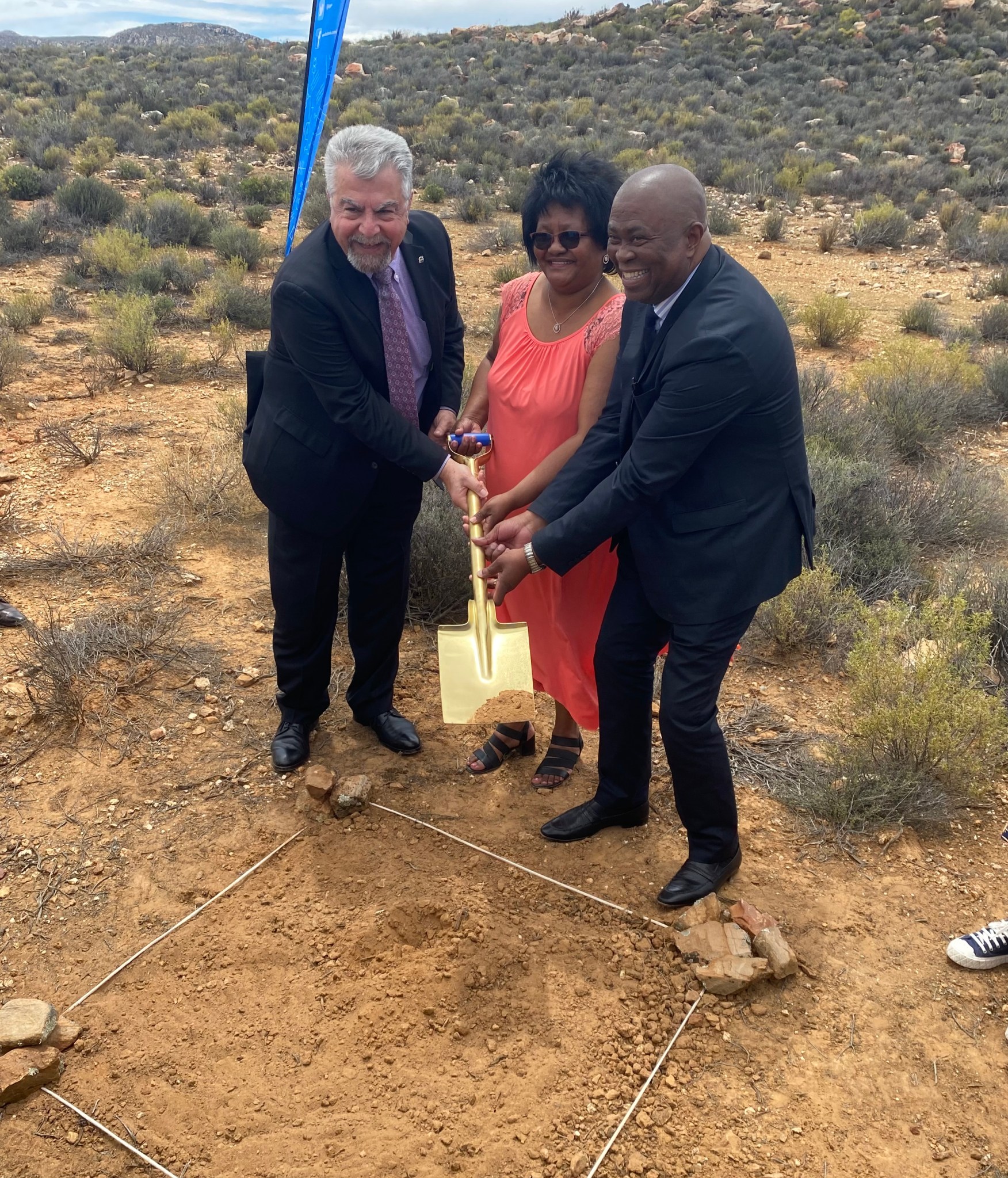 In this image, three people hold a gold shovel in a groundbreaking ceremony in Matjiesfontein, South Africa.