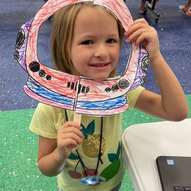 A young woman envisions a future as an astronaut holding a helmet-on-a-stick in front of her face during her NASA’s ASTRO CAMP® Community Partners (ACCP) activity with community collaborator Central Creativity.