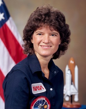 Sally Ride poses for her official NASA Astronaut portrait with the American flag and a Space Shuttle model in the background