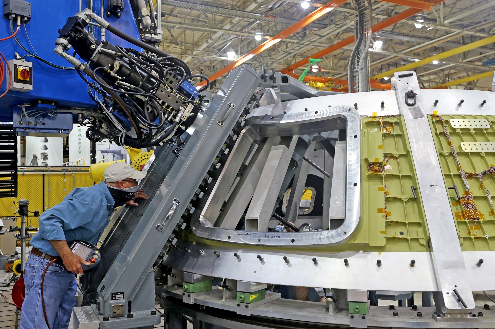 A man leans forward as a machine welds parts of the Orion crew module together.