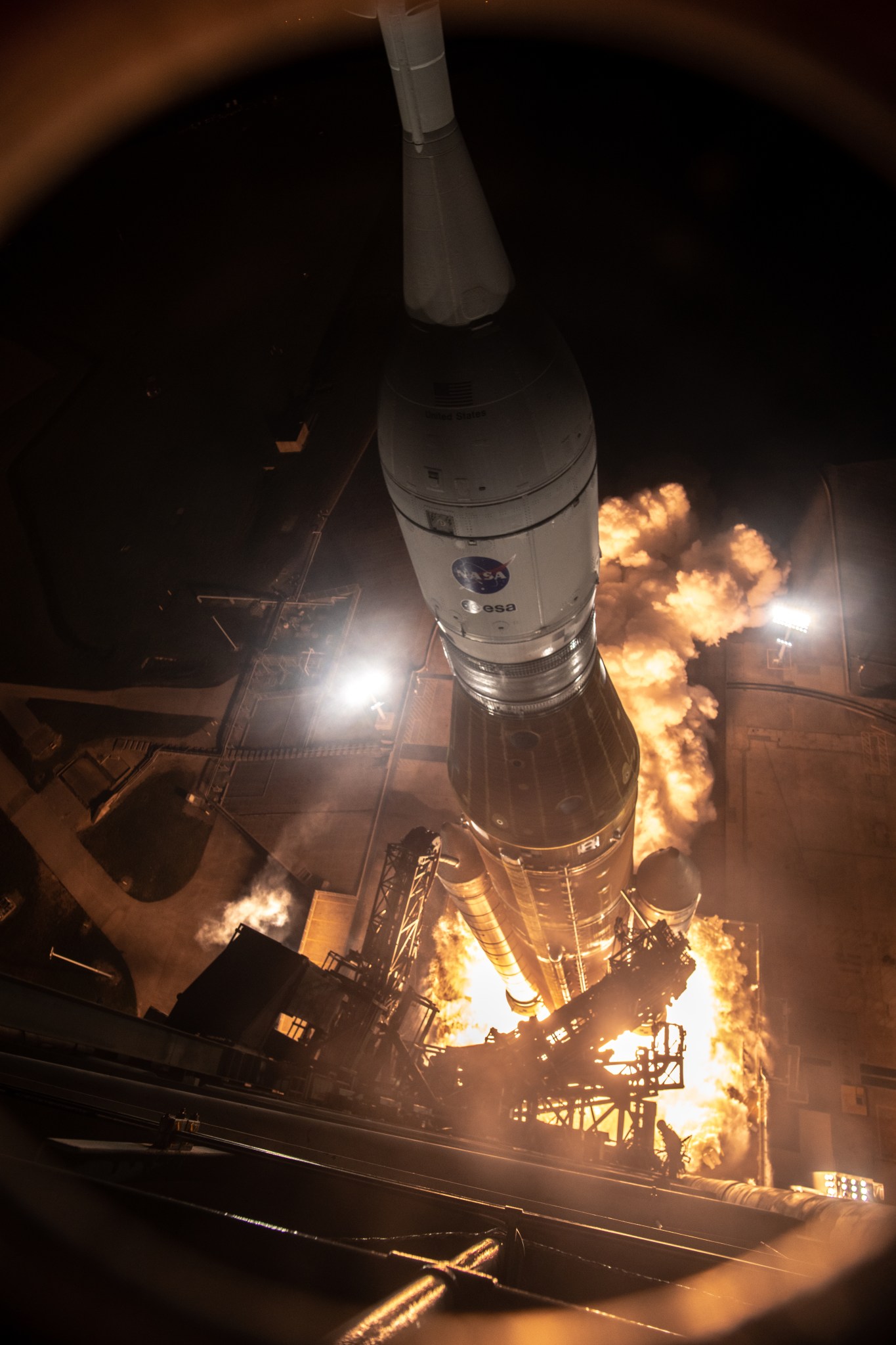 A bird's eye view from high up on the mobile launcher shows the Space Launch System rocket's liftoff. Fire from the engines can be seen.