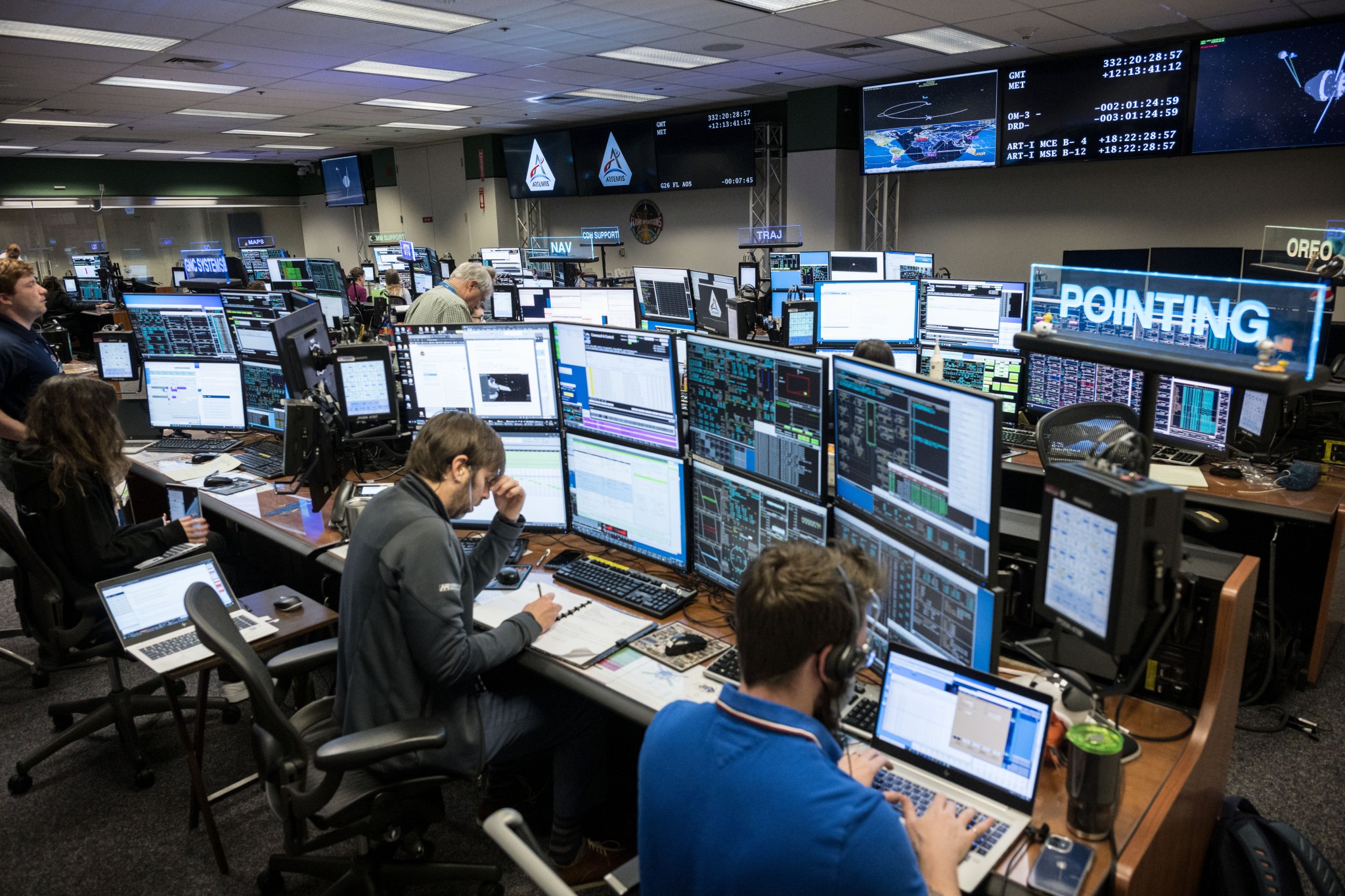 Flight controllers in a room in mission control at Johnson Space Center in Houston monitor the Artemis I mission, with multiple screens showing data for person in the room. 