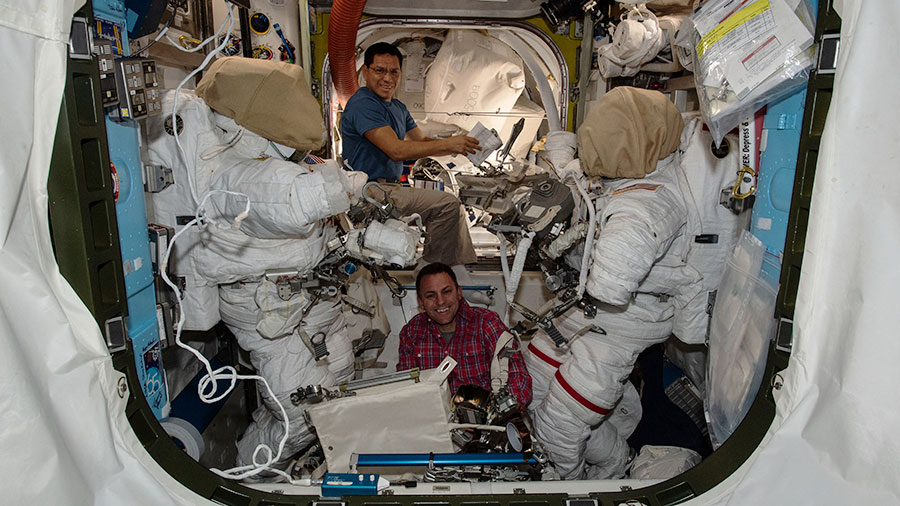 Astronauts (from top) Frank Rubio and Josh Cassada work on a pair of Extravehicular Mobility Units (EMUs), or spacesuits, inside the space station's Quest airlock.
